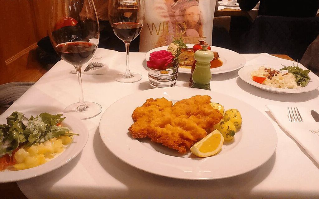 Plate of Wiener schnitzel with potatoes and glasses of wine.