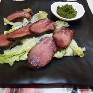 Corned tongue slices on a bed of lettuce with a bowl of green chutney.