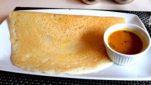 Dosa on a white plate with a bowl of sambar.