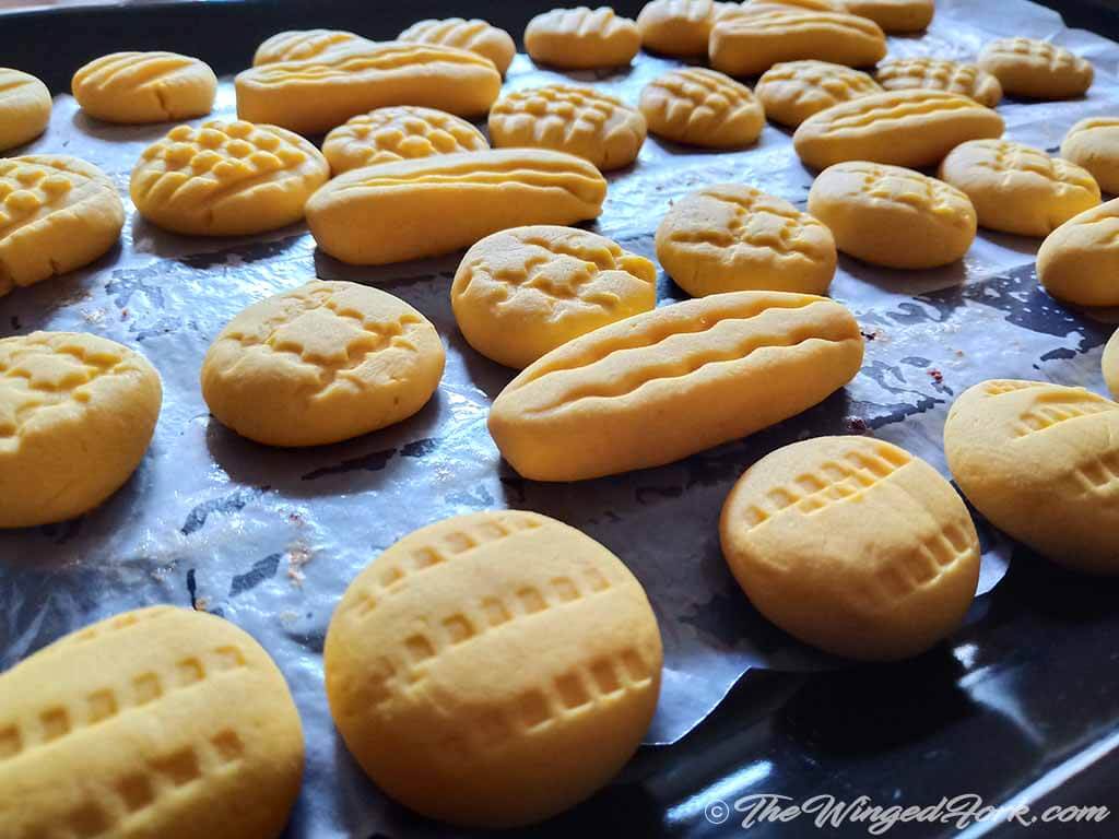Freshly baked yellow colour custard powder cookies cooling on a tray.