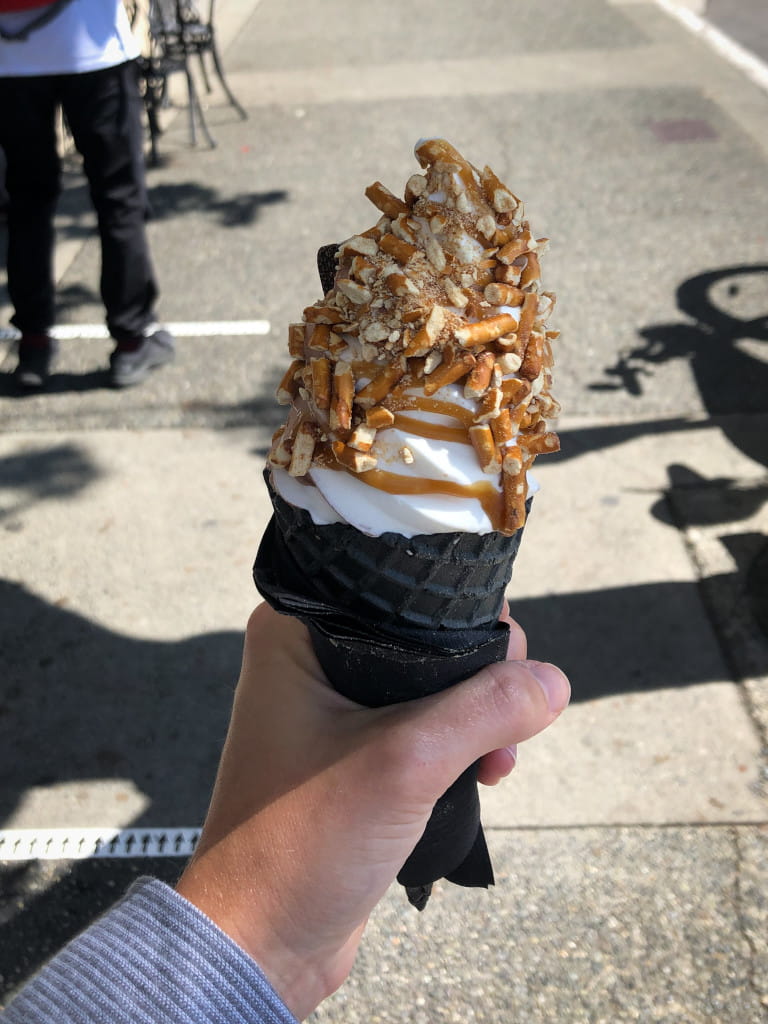 Black ice cream cone with soft serve and brown crunchy topping.