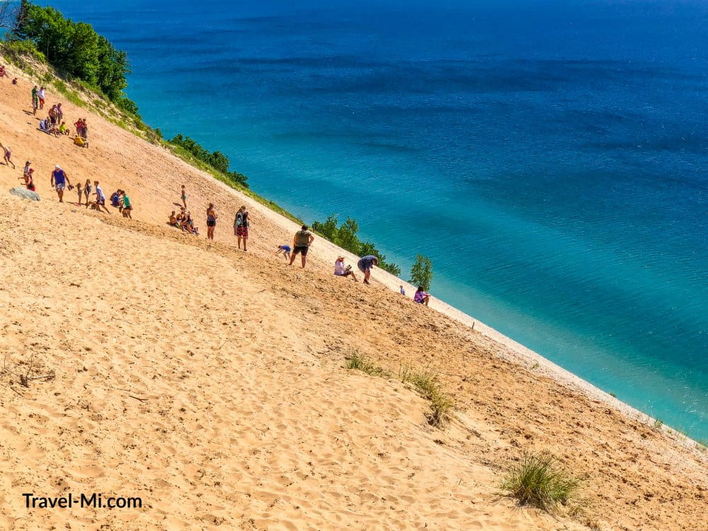 People sitting on sleeping bear dunes in front of Lake Michigan.