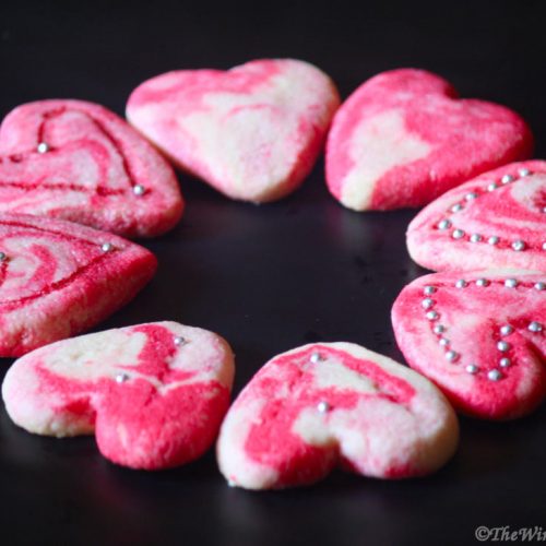 Pink and white heart cookies on a black surface.