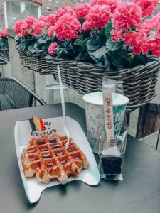 Picture of Belgian waffles and coffee with flowers in the background by Mayuri of To Some Place New.