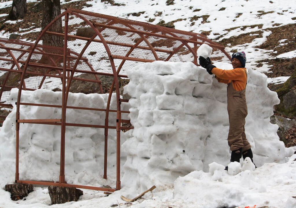 Man placing ice blocks on large igloo frame.