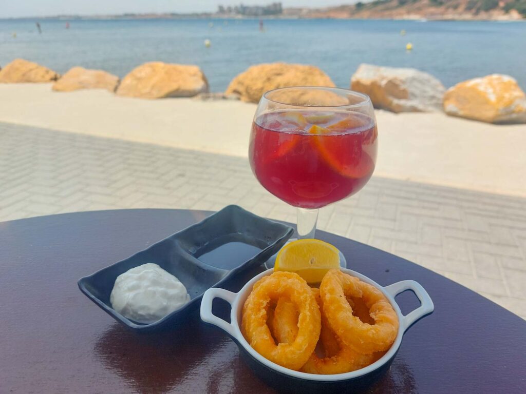 Calamari and Aioli with a glass of Sangria on a beachside table.