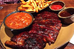 Barbecue ribs, beans, French fries and sauces served on plate.