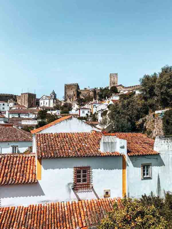 Whitewashed houses and view of the wall and Óbidos Castle in the background.