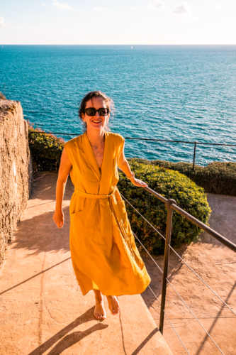 Lady in yellow dress on stone staircase near sea.